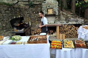 Um espaço ao ar livre com churrasqueira, forno de pedra e diversos alimentos dispostos em mesas.