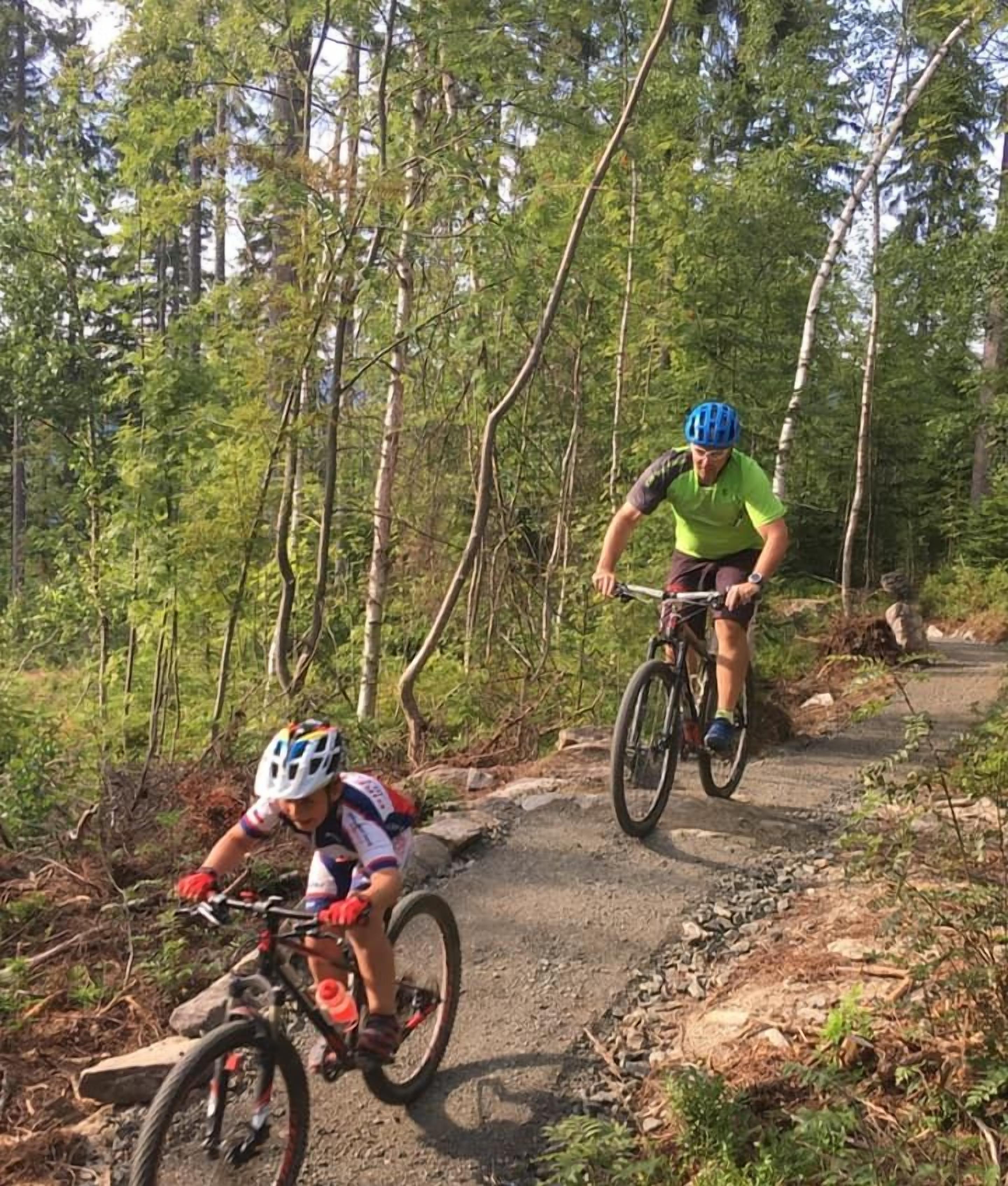 Two cyclists on a dirt trail surrounded by trees.