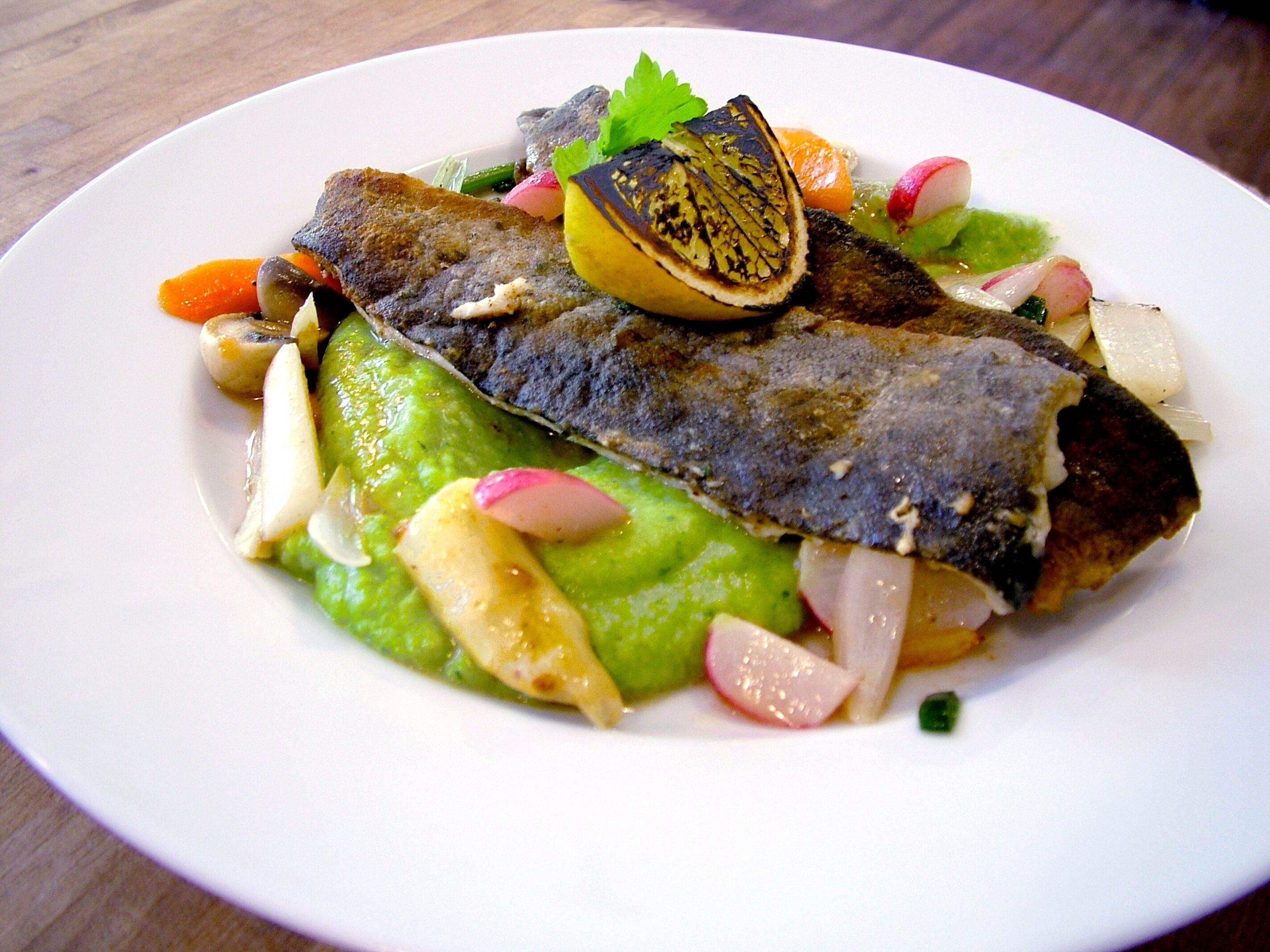 Un plato de comida con pescado, aguacate, rábano y limón.