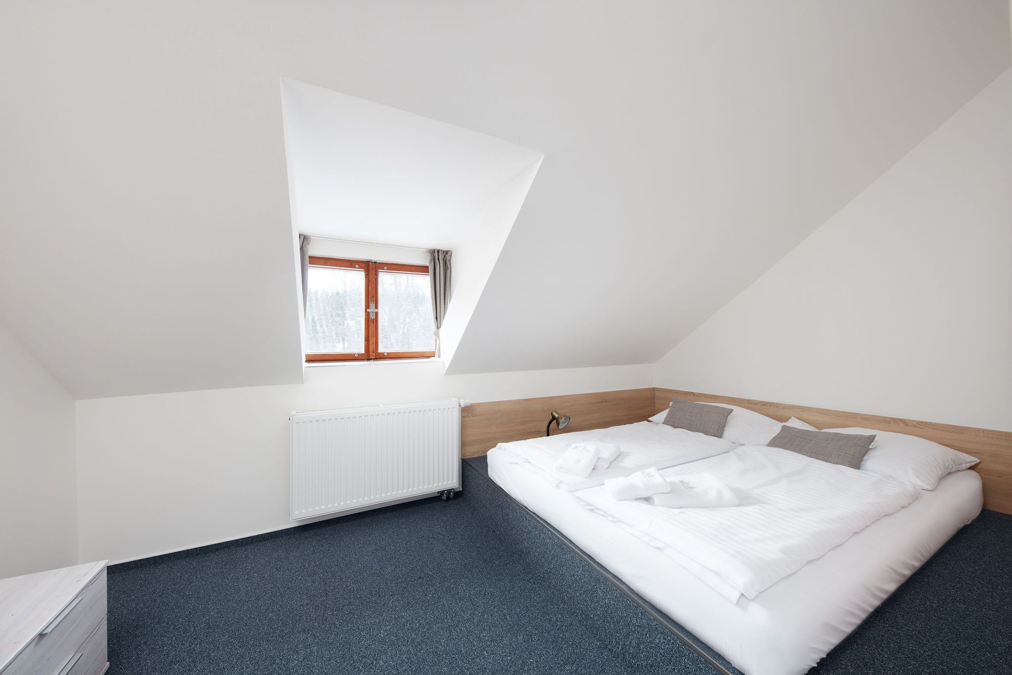 Un dormitorio con techo inclinado, una cama individual, un radiador y una ventana con cortinas.