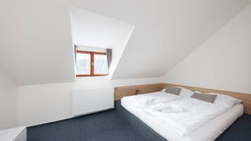 Un dormitorio con techo inclinado, una cama individual, un radiador y una ventana con cortinas.