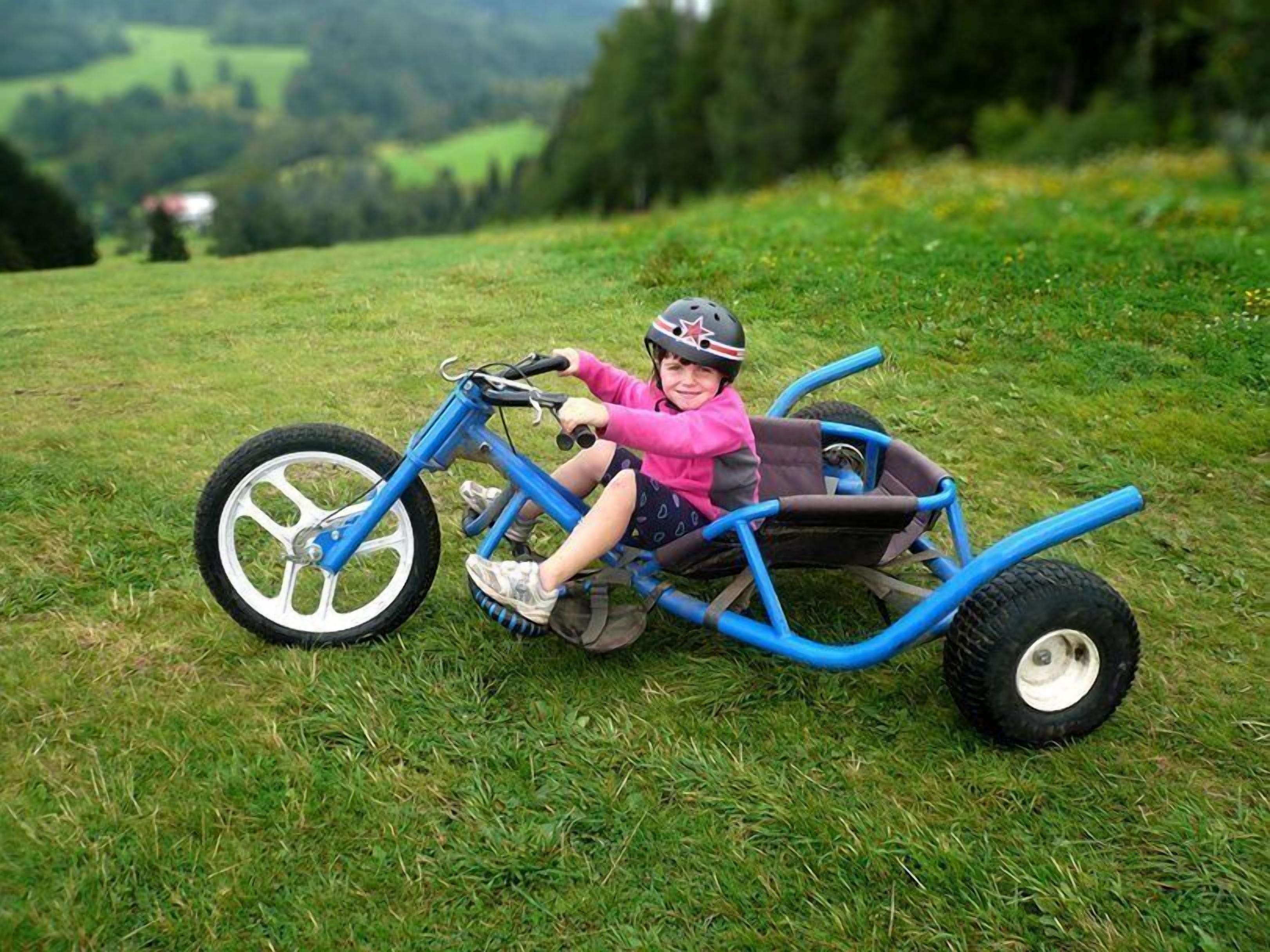 A child riding a blue tricycle with a sidecar on a grassy field.