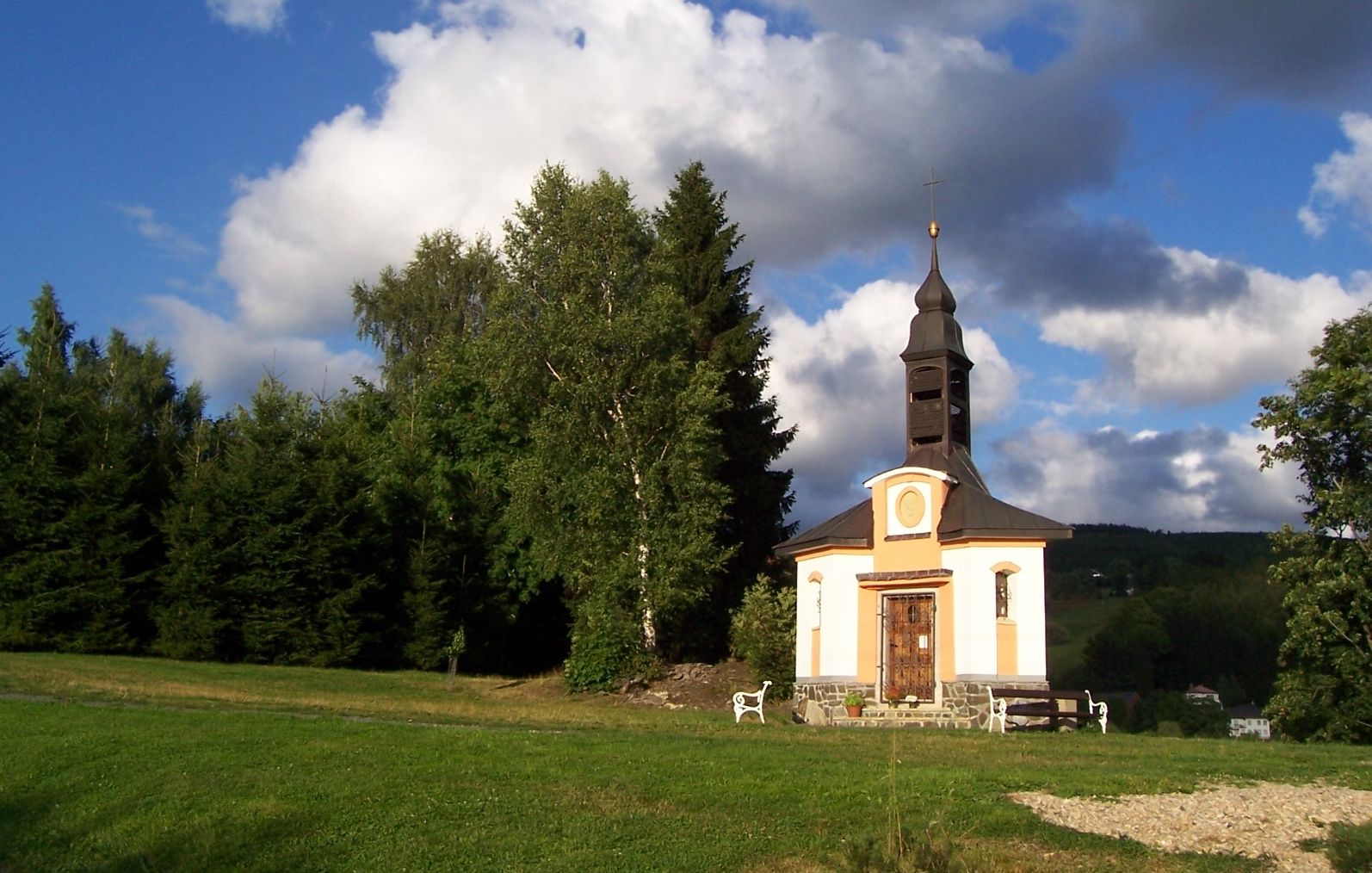 A small church with a bell tower, surrounded by trees and a grassy field.