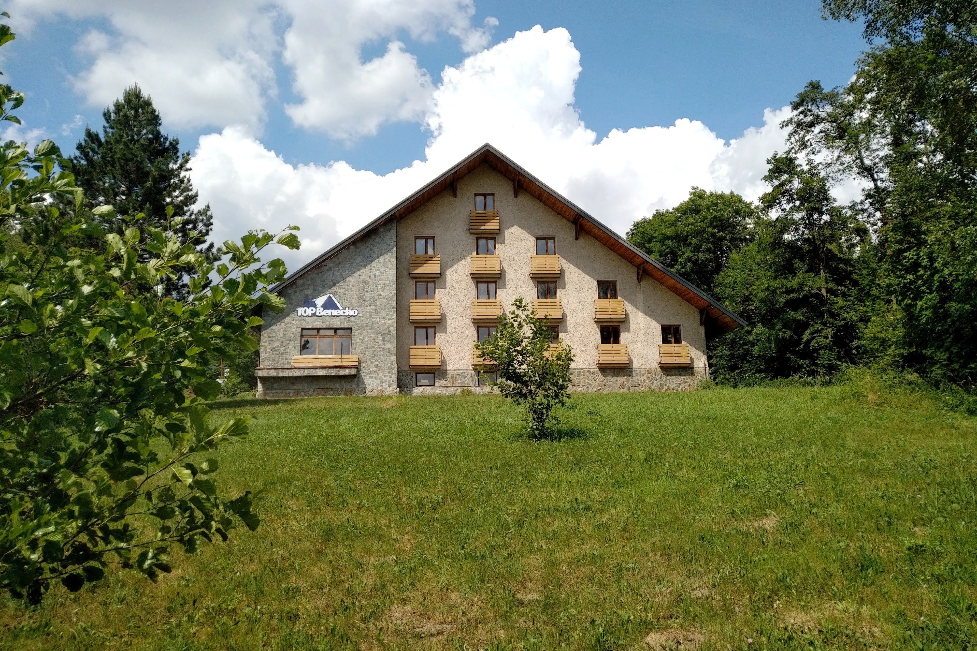 A stone building with wooden balconies, a grassy lawn, and trees in the background.