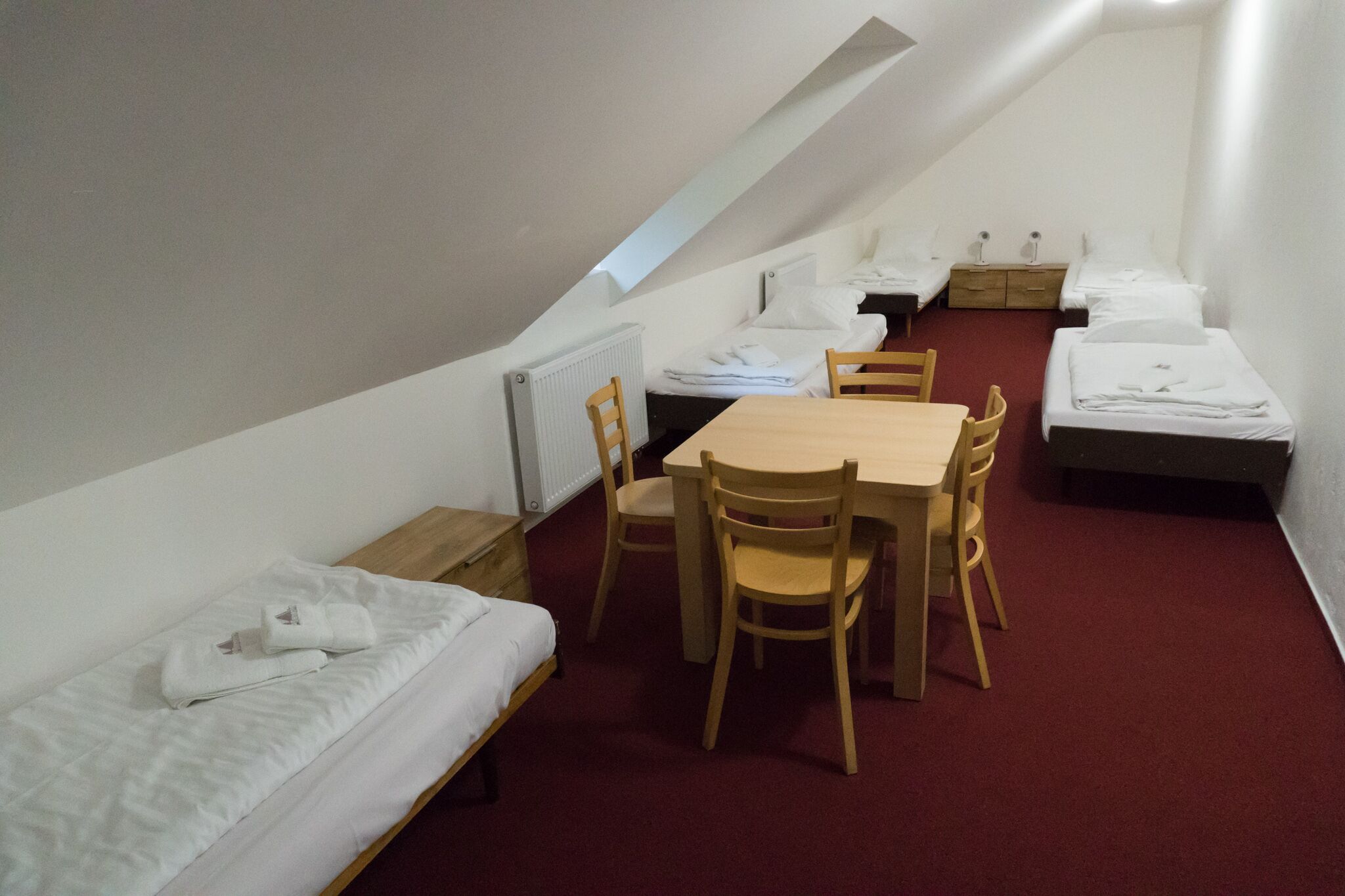 A dormitory room with a single bed, a table with chairs, and a second bed in the background.