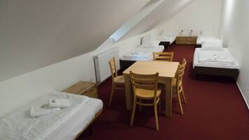 A dormitory room with a single bed, a table with chairs, and a second bed in the background.