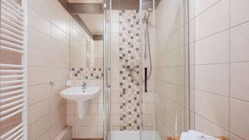 A bathroom with a glass-enclosed shower, a sink, and a wooden bench.