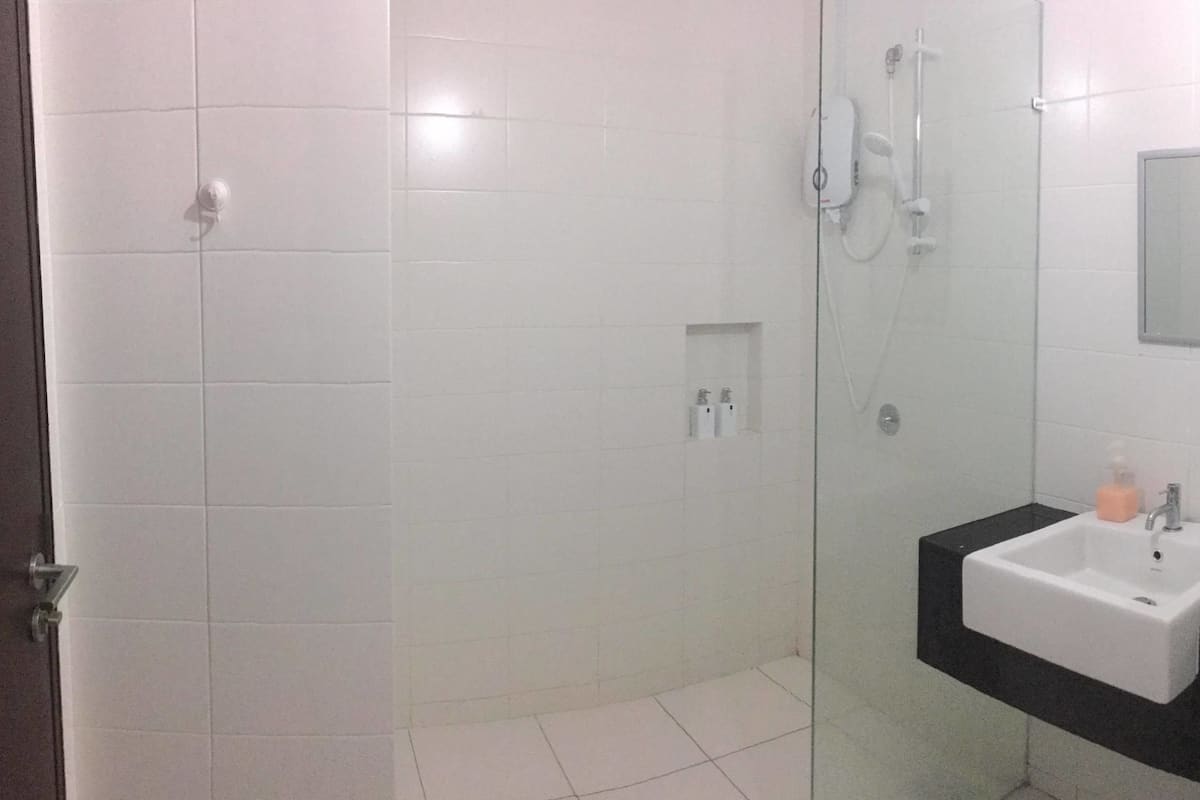 Un bany amb rajoles blanques, un box de dutxa de vidre, un lavabo amb taulell negre i un mirall a la paret.