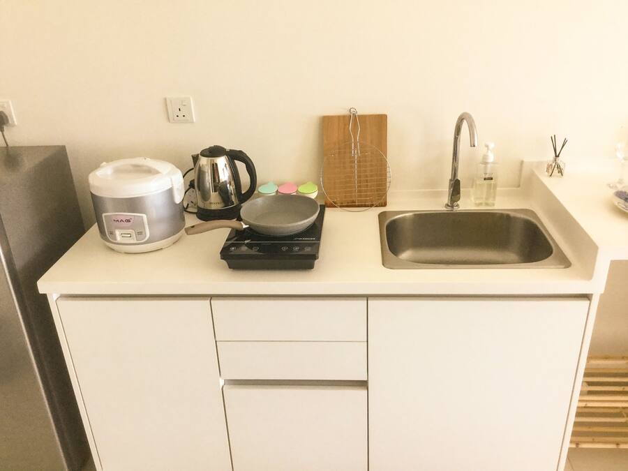 A compact kitchen with a coffee maker, a frying pan on a portable stove, a kettle, and a sink.