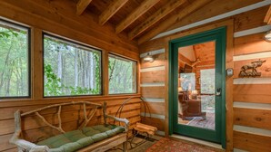 A log cabin interior with a wooden bench, large windows, a green door, and a patterned rug. - Creek-front Cabin on Wooded Acres (Sugar Grove)