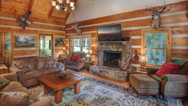 A log cabin interior with a fireplace, wooden furniture, and mounted animal heads. - Creek-front Cabin on Wooded Acres (Sugar Grove)