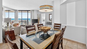 A dining area with a glass table, wicker chairs, and a hanging lamp.