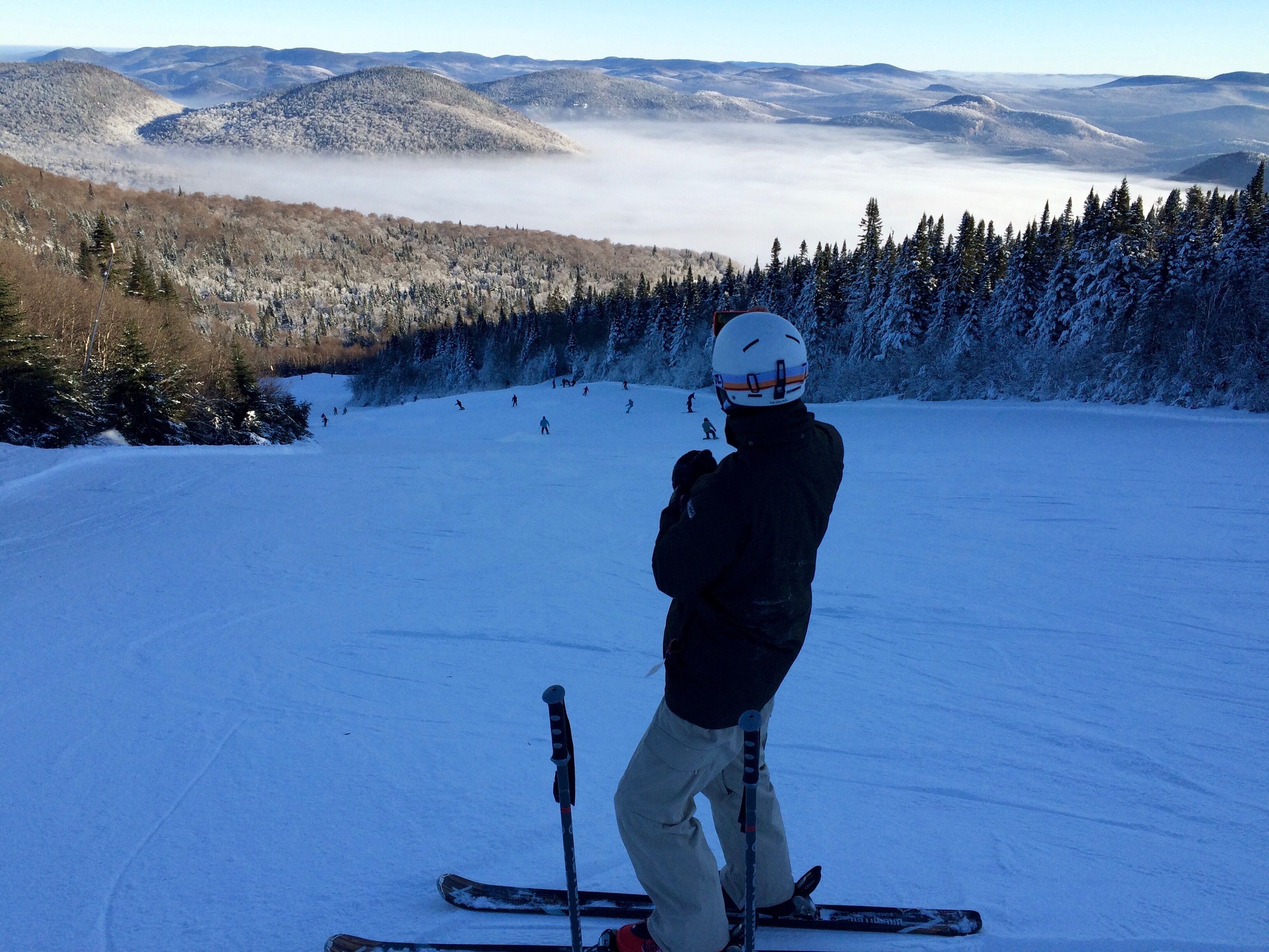 Une personne fait du ski sur une pente enneigée, avec une montagne boisée en arrière-plan.