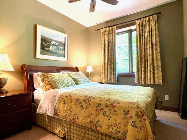 A bedroom with a bed, nightstands, a ceiling fan, a window with curtains, and a framed picture on the wall.