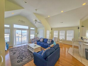 A spacious living room with a high ceiling, a ceiling fan, and a view through large windows.