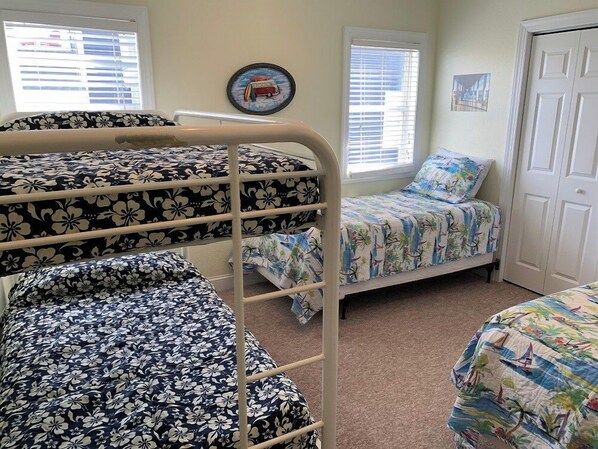 A bedroom with bunk beds, a window with blinds, a door, and a wall with a picture.