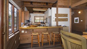 Une cuisine avec des tabourets de bar en bois, une grande fenêtre et une vue sur l’extérieur.