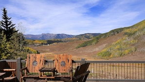 Une terrasse en bois, dotée de chaises Adirondack, offrant une vue sur un paysage montagneux.