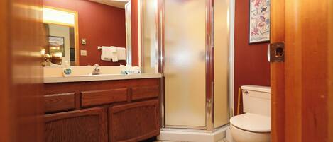 A bathroom with a wooden vanity, a glass shower enclosure, and a toilet.