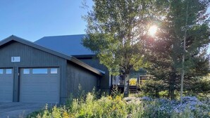 A building with a garage door, surrounded by a garden with various plants and flowers. - Mt CB Home | 3 Bedroom | Hot Tub | Gas Grill | Mt CB View | Second Living Room (Mt. Crested Butte)