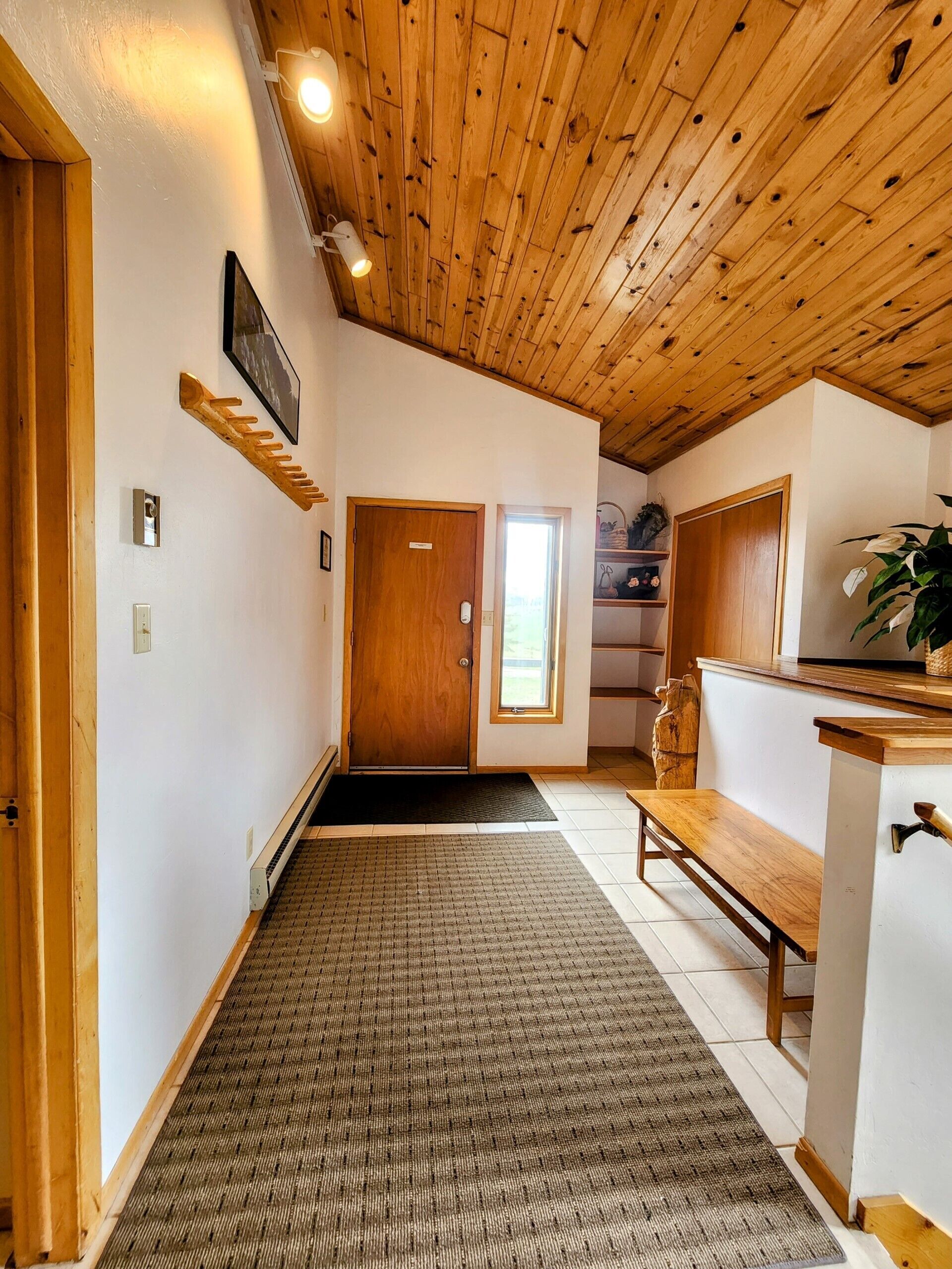 Un corridoio con soffitto in legno, una panca, una porta e una piccola finestra.