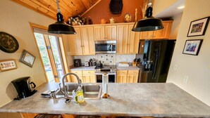 A kitchen with wooden cabinets, a large island with bar stools, stainless steel appliances, and pendant lighting. - Mt CB Home | 3 Bedroom | Hot Tub | Gas Grill | Mt CB View | Second Living Room (Mt. Crested Butte)