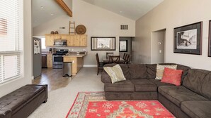 A spacious living area with a brown sectional sofa, a red patterned rug, and a dining table with chairs.