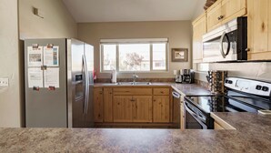 A kitchen with wooden cabinets, a stainless steel refrigerator, a microwave, a stove, and a window providing natural light.