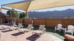 A patio with lounge chairs and a large canopy, overlooking a mountainous landscape.