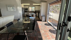 A modern kitchen with white cabinets, a stainless steel refrigerator, and a microwave. There is a dining area with a glass table and chairs. - ☀️PERFECT LOCATION, SPACIOUS and affordable! SOUTH MISSION BEACH Steps to Ocean! (San Diego)