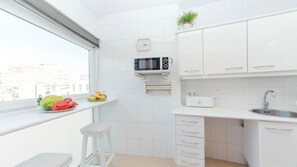 Une cuisine moderne avec des meubles blancs, un four à micro-ondes, un évier et une fenêtre donnant sur des immeubles.