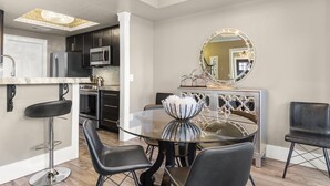 Une cuisine moderne avec des meubles de couleur sombre, des appareils en acier inoxydable et une table à manger en verre, assortie de chaises noires.