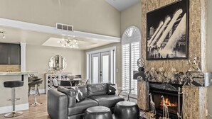 Un salon moderne avec un canapé d’angle, des poufs noirs, une cheminée et un coin repas comprenant une table ronde et des chaises.