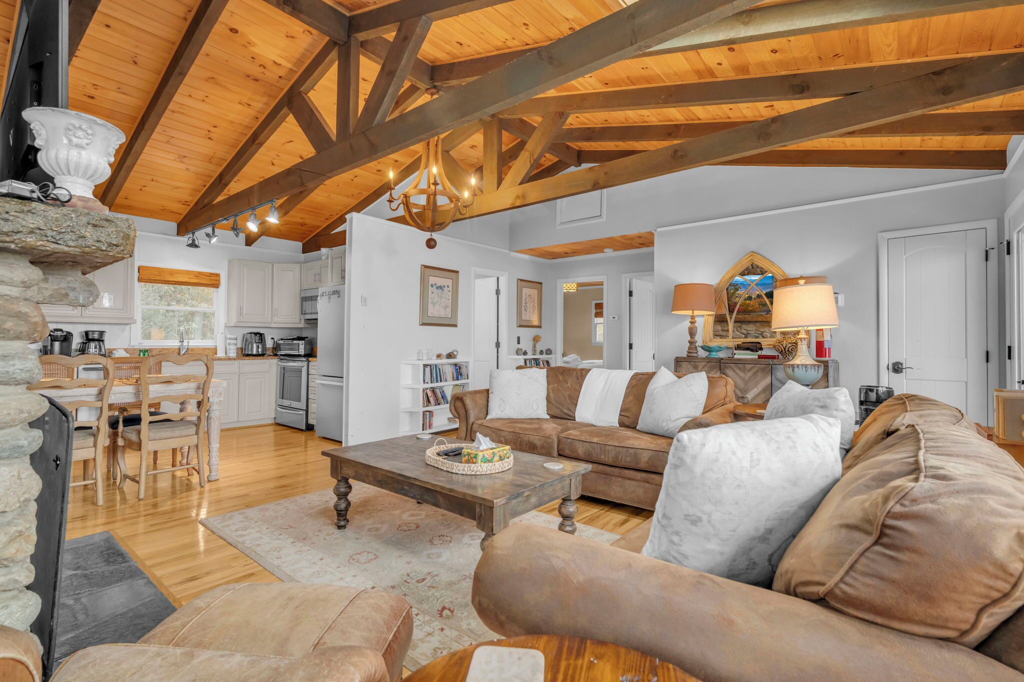 A spacious living area with a wooden ceiling, a cozy sofa, a dining table, and a kitchen in the background.