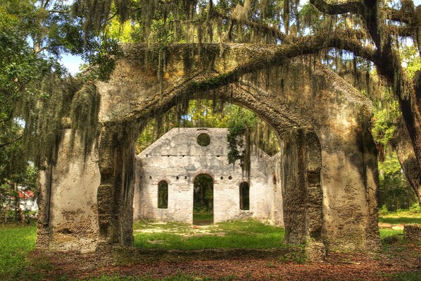 Un edificio antiguo de piedra con arcos en puertas y ventanas, rodeado de árboles y pilares de piedra cubiertos de musgo.