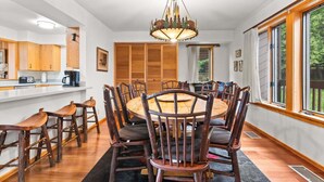 A dining room with a round table, wooden chairs, a chandelier, and large windows. - RMR: Wind River 10 Condo in Teton Village (Teton Village)