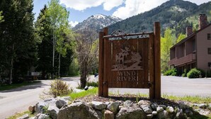 A wooden sign with 'Wind River' and a moose illustration, surrounded by trees and a mountain in the background. - RMR: Wind River 10 Condo in Teton Village (Teton Village)