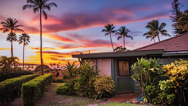 Une maison avec un jardin, des palmiers et un coucher de soleil.