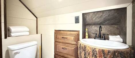 A bathroom with a toilet, a wooden vanity with a sink, and a mirror.