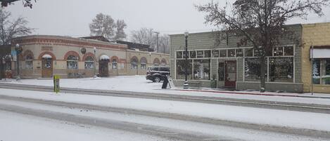 A building with a brick facade and arched windows, a parked car, and a snow-covered street.