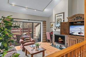 A cozy living room with a fireplace, a television, and a sliding glass door leading to an outdoor area. - RMR: Cinquefoil 1614 Condo in The Aspens/Wilson,WY (Wilson)