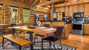 A log cabin interior with a dining area, kitchen, and large windows. - RMR: Granite Ridge Cabin 7586 in Teton Village (Teton Village)
