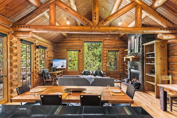 A log cabin interior with a dining area, seating, a fireplace, and a television.