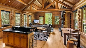 A log cabin interior with a kitchen, dining area, and living room, featuring large windows and wooden beams. - RMR: Granite Ridge Cabin 7586 in Teton Village (Teton Village)
