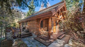 A log cabin with a stone foundation, wooden deck, and a mountain backdrop. - RMR: Granite Ridge Cabin 7586 in Teton Village (Teton Village)