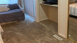 A bedroom with a bed, a TV on a stand, a window with blinds, and a carpeted floor. - Las Palmas resort ground floor 3 bedroom condo large couch seating hottubs pools (St George)
