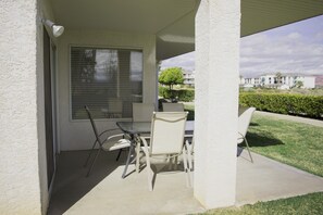 A covered patio with a table and chairs, a window with blinds, and a view of a residential area. - Las Palmas resort ground floor 3 bedroom condo large couch seating hottubs pools (St George)