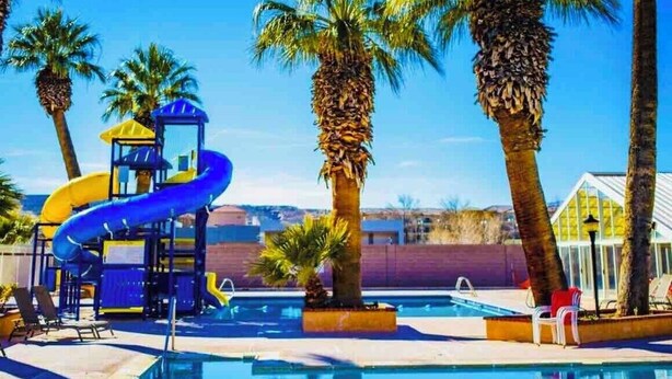 A swimming pool with a blue slide, palm trees, and lounge chairs. - Las Palmas resort ground floor 3 bedroom condo large couch seating hottubs pools (St George)