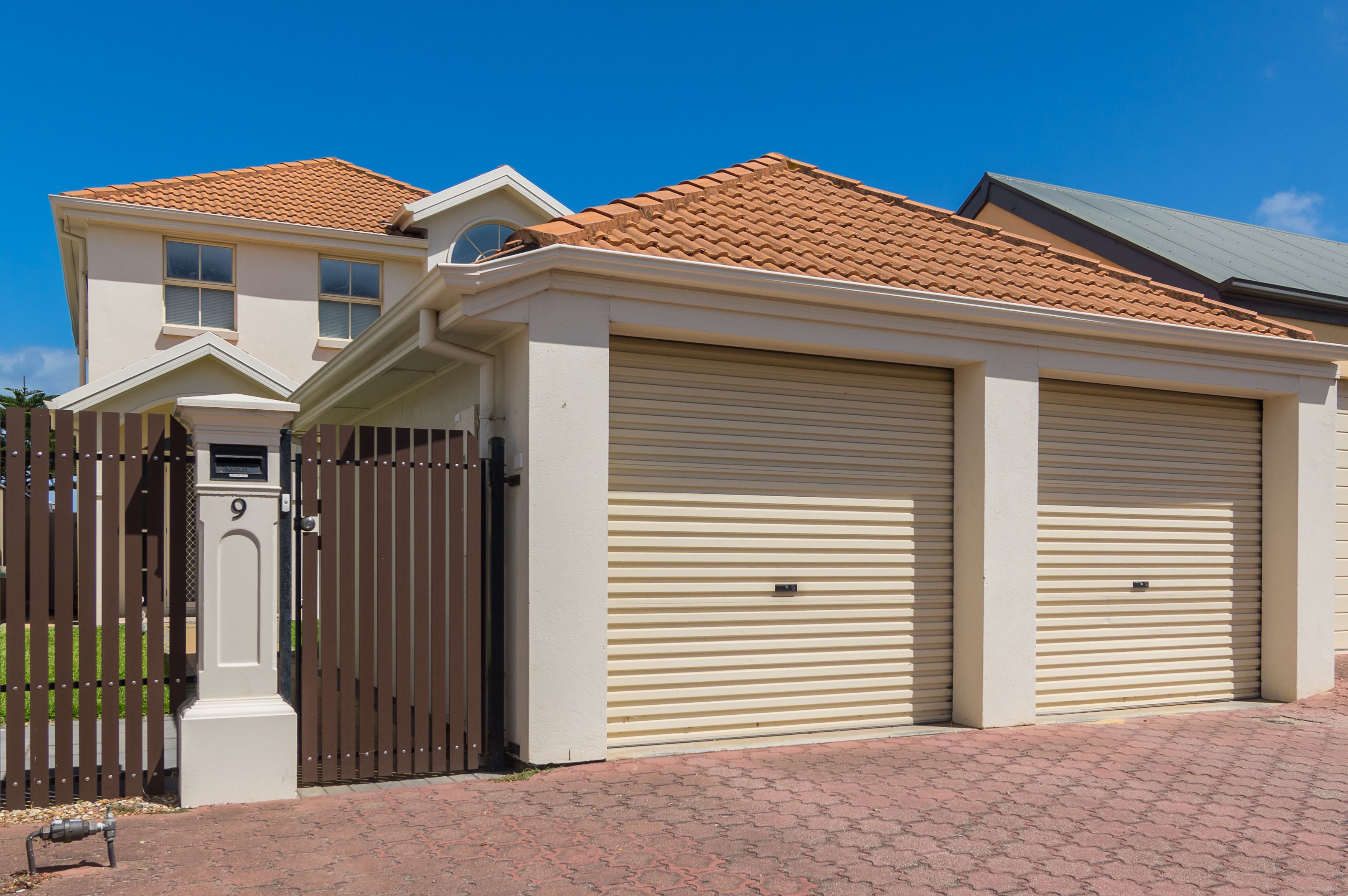 A two-story house with a brown gate, beige garage doors, and a red-tiled roof.