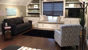A cozy living room with a dark-colored sofa, a patterned armchair, and a built-in bench with storage shelves.